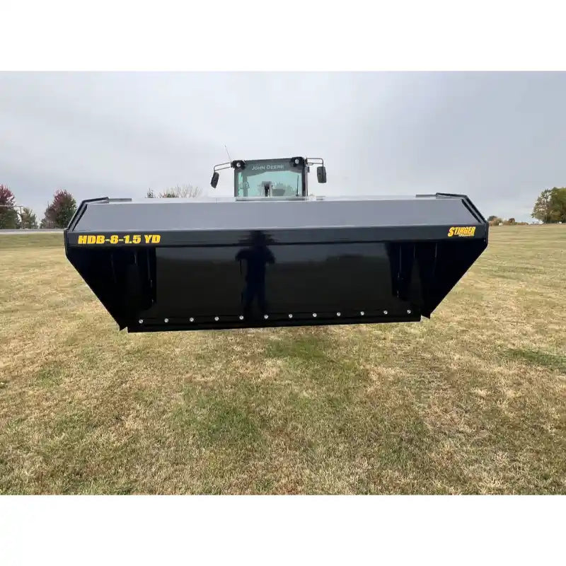 Front view of black steel hydraulic dump bucket attachment elevated in front of a tractor on grassy field