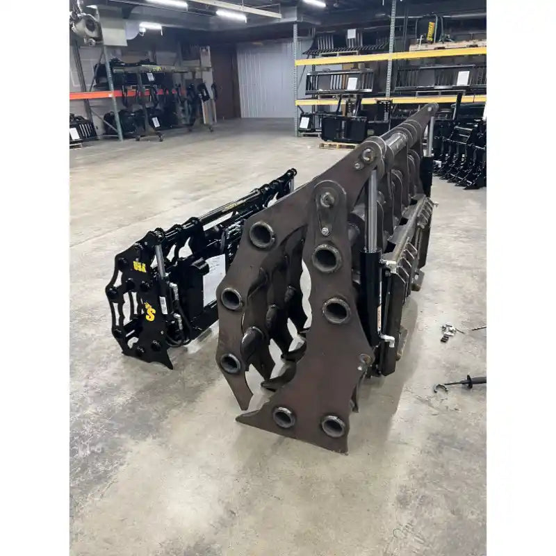 Two heavy steel clam grapple attachments with multiple mounting holes arranged on a concrete floor inside a warehouse