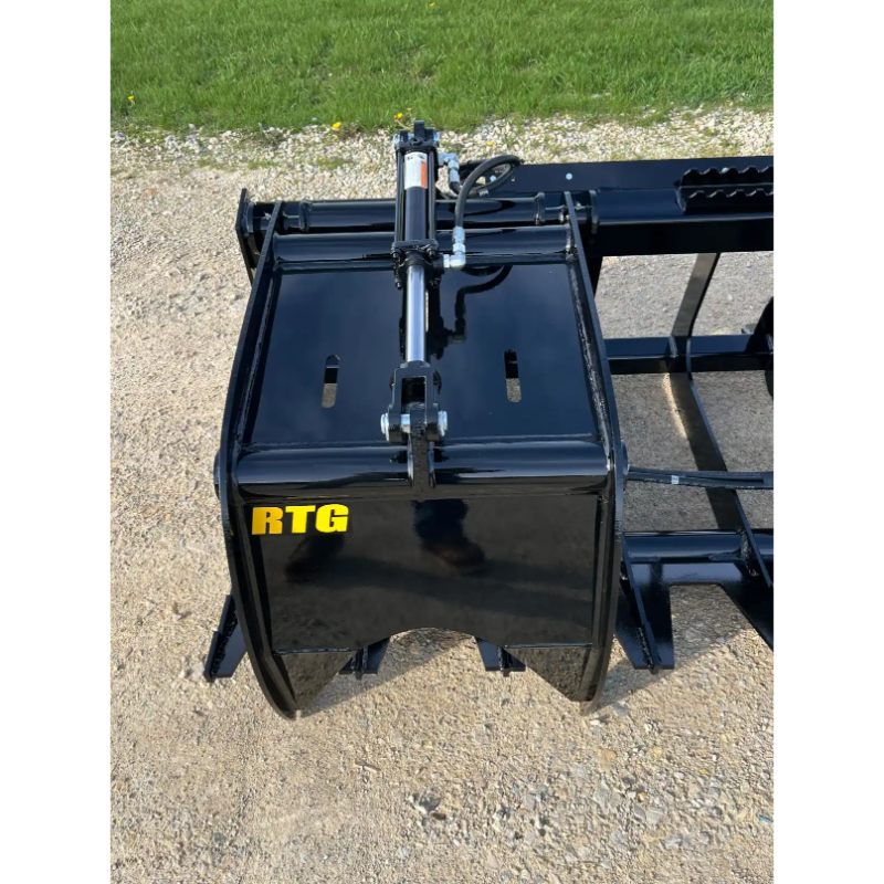 Black skid steer root grapple bucket with hydraulic cylinder and mounting bracket on gravel surface