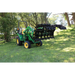 Green compact tractor fitted with extended black steel grapple attachment holding sticks on grass outdoors
