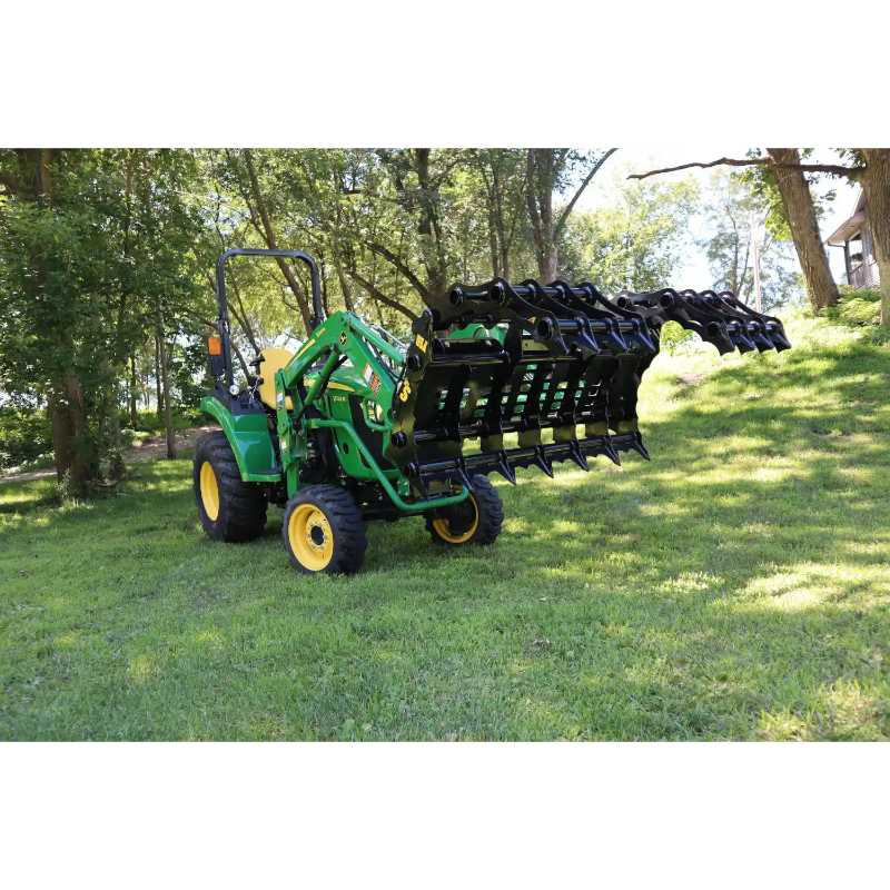 Green compact tractor fitted with extended black steel grapple attachment holding sticks on grass outdoors