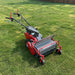 Red walk-behind flail mower on grass with front mesh shield, caster wheels, and control handlebars