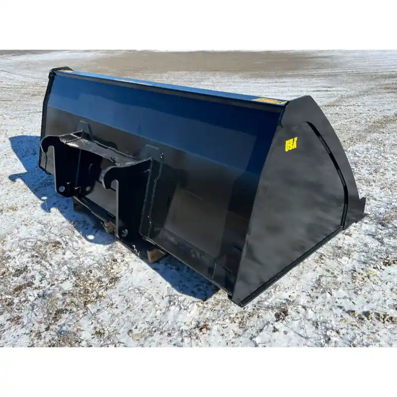 Right side view of black steel skid steer bucket attachment resting on snow-covered gravel surface outdoors