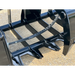 Close-up of curved black skid steer root grapple teeth and frame with hydraulic hose on gravel surface