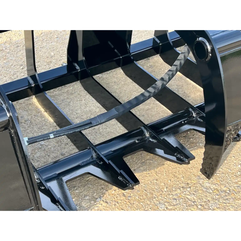 Close-up of curved black skid steer root grapple teeth and frame with hydraulic hose on gravel surface