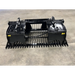 Black skid steer rock grapple attachment with dual hydraulic cylinders, wide serrated tines, and reinforced arms on concrete floor