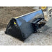 Side view of black steel skid steer bucket attachment positioned on concrete near mulch pile