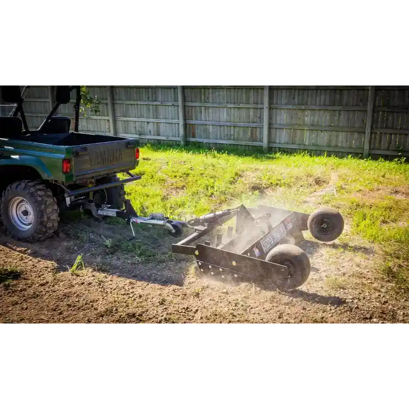 Swisher 48-inch driveway grader attached to ATV, angled side view, clearing dirt and leveling ground, gallery position 1