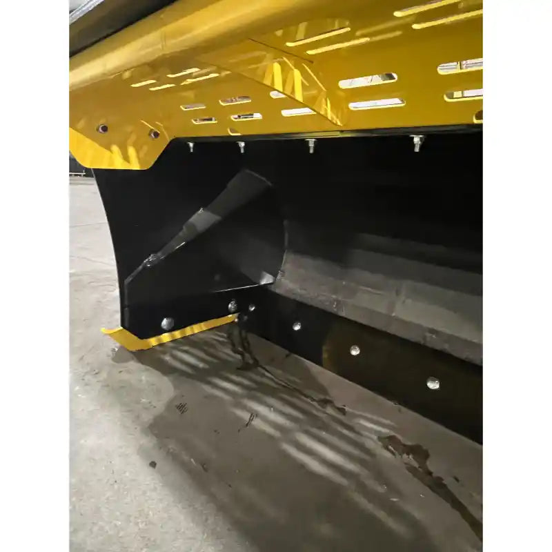 Close-up of yellow and black steel snow pusher attachment showing wear strip and mounting bolts on concrete floor