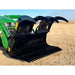 Black steel grapple attachment with serrated clamshell jaws and wide curved tines mounted on green tractor loader arm