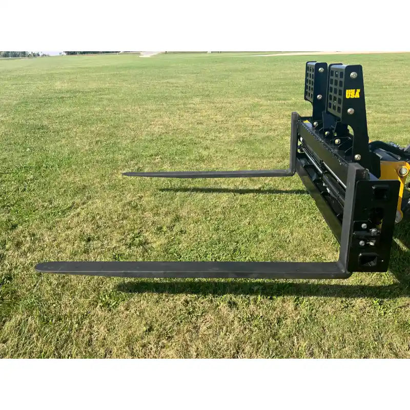 Black steel pallet fork attachment with solid rectangular backrest and two long fork tines on grass field outdoors
