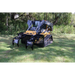 Skid steer loader equipped with black metal rock grapple attachment with spaced tines sitting on grass near trees