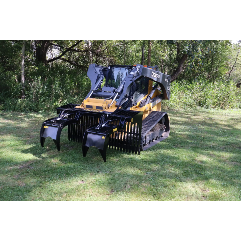Skid steer loader equipped with black metal rock grapple attachment with spaced tines sitting on grass near trees