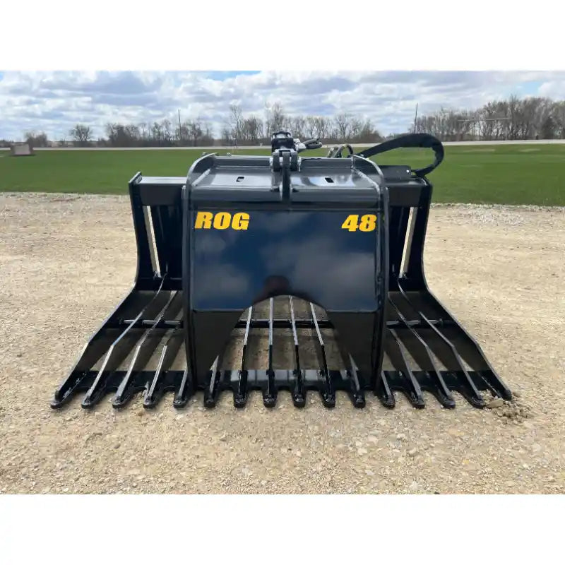 Front view of black metal skid steer rock grapple attachment with wide spaced curved tines and hydraulic hoses on gravel surface