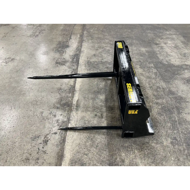 Black metal bale spear attachment with two long pointed spears on concrete floor