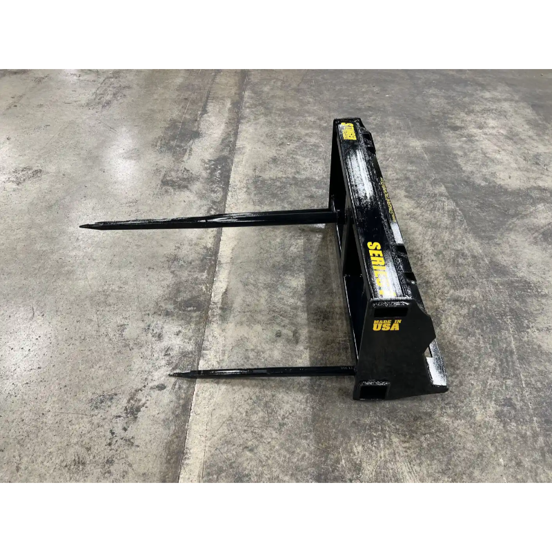 Black metal bale spear attachment with two long pointed spears on concrete floor