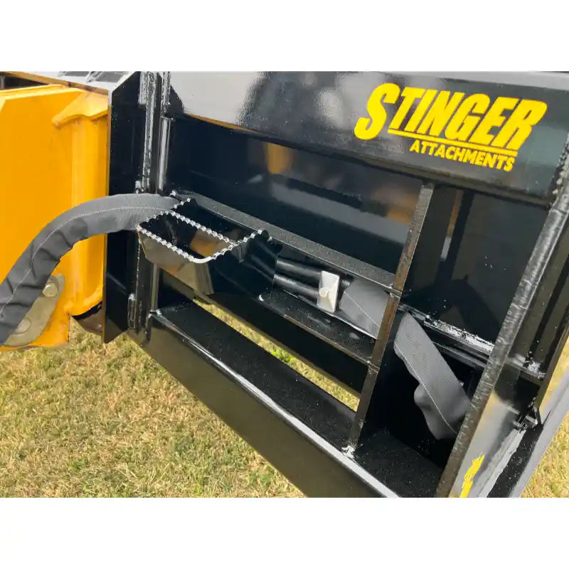 Close-up of black painted steel hydraulic attachment frame with protective hose covers and yellow Stinger Attachments logo over grass