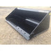 Left-front angled view of black steel skid steer bucket with bolt-on edge on compacted dirt surface