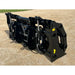 Black steel clam grapple attachment with hydraulic lines and reinforced frame resting on gravel outdoors