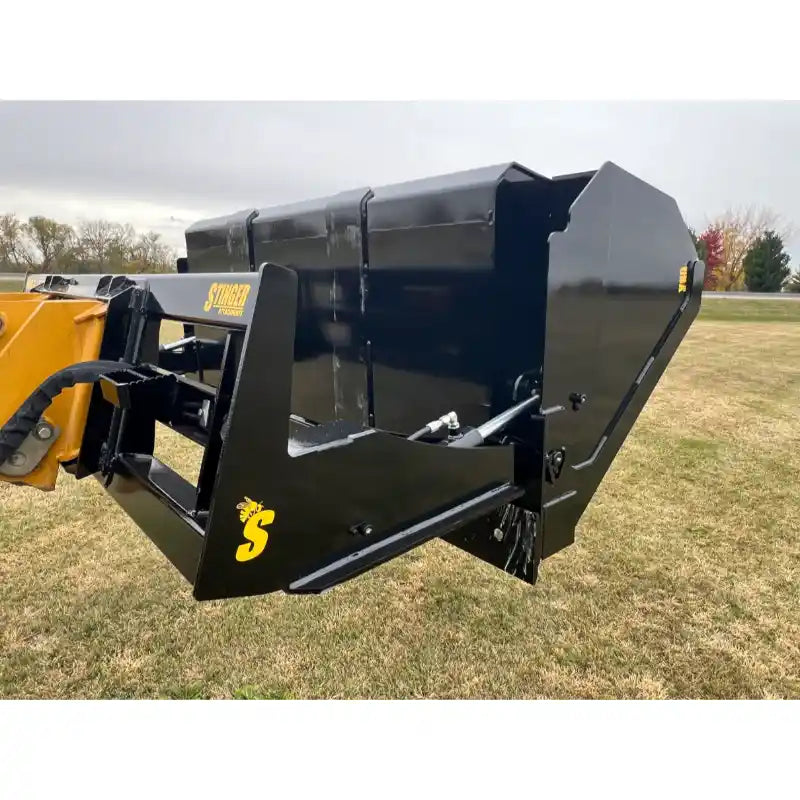 Black steel tractor hydraulic dump bucket attachment tilted back with visible tipping mechanism and mounting frame on grass field