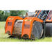 Orange steel grapple attachment with American flag decals gripping a large weathered log on a compact loader outdoors