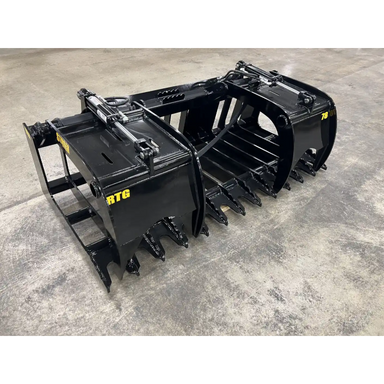 Black steel skid steer grapple attachment with dual hydraulic cylinders, curved tines, and reinforced frame on concrete floor