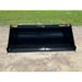 Black steel skid steer material bucket with smooth interior and yellow Stinger Series 1 72 lettering outdoors on gravel and grass