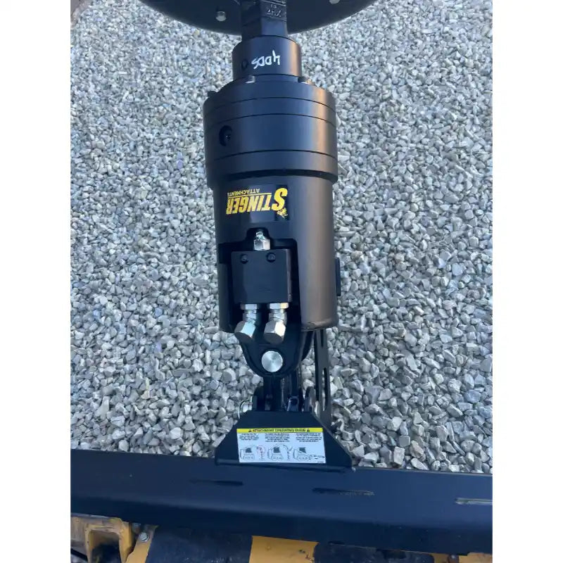 Black hydraulic drive motor with yellow Stinger logo and hydraulic hoses mounted on loader attachment over gravel