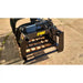 Black painted steel manure tine grapple attachment with hydraulic cylinders and horizontal tines on concrete surface outdoors