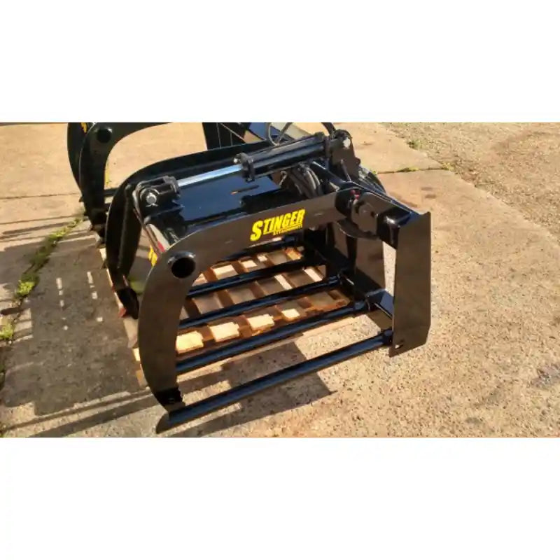 Black painted steel manure tine grapple with horizontal spaced tines and dual hydraulic cylinders on concrete surface outdoors
