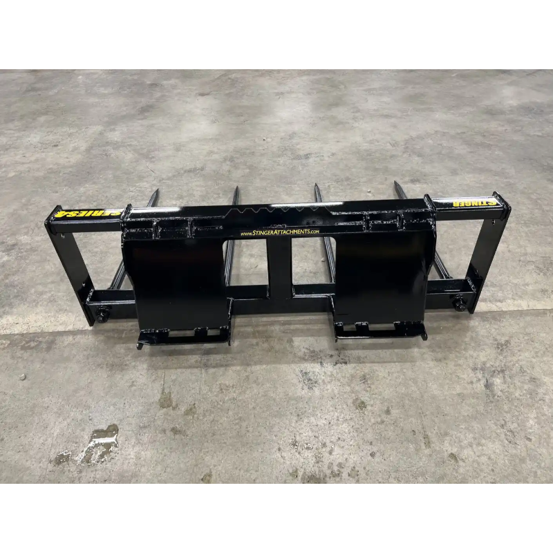 Black steel bale spear skid steer attachment with four pointed tines and mounting brackets viewed from back on concrete floor