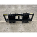 Black steel skid steer bale spear attachment with four tines and reinforced mounting plates on concrete floor viewed from rear angle