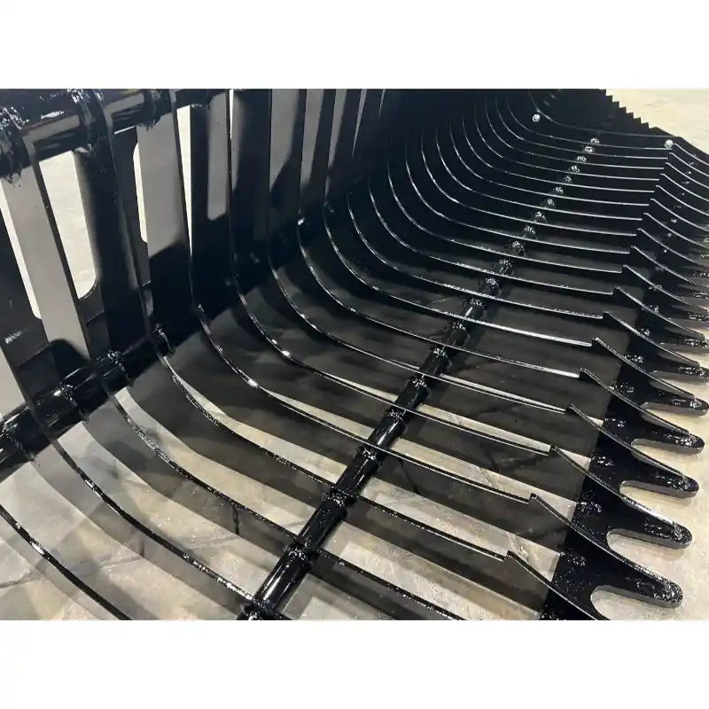 Close-up of black metal rock bucket attachment with curved teeth and reinforced crossbars on concrete floor
