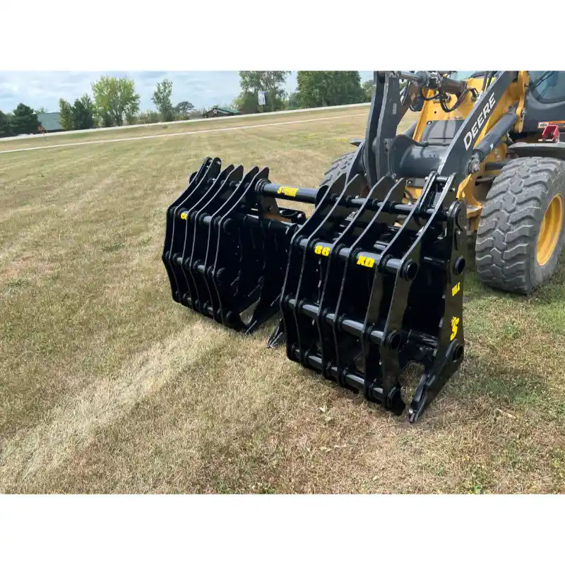 Black steel skid steer grapple attachment with multiple curved tines mounted on yellow loader over dry grass field