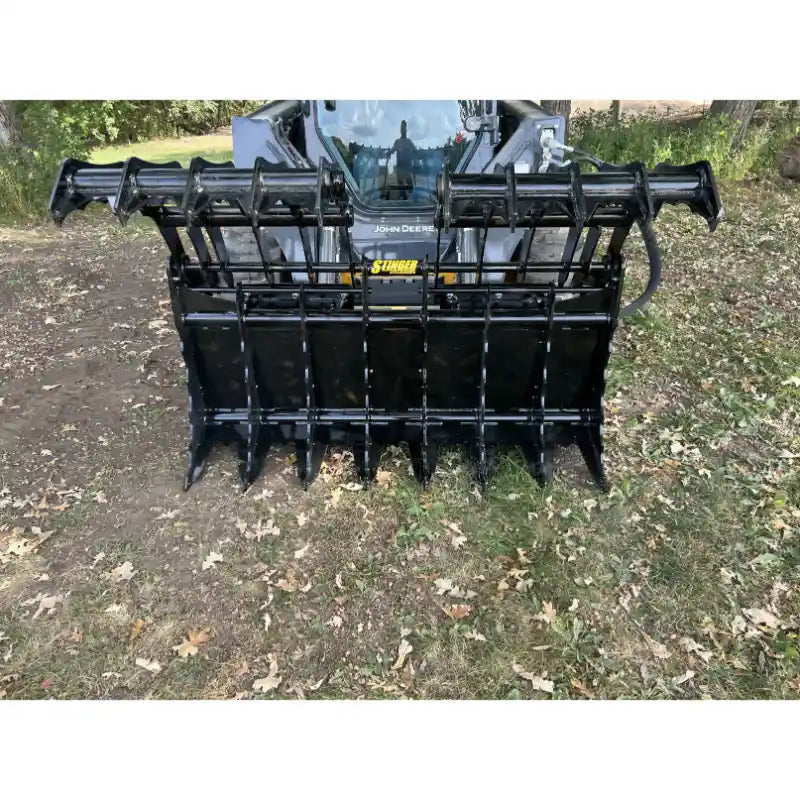 Front view of black steel clam grapple attachment with open jaws mounted on skid steer in outdoor setting