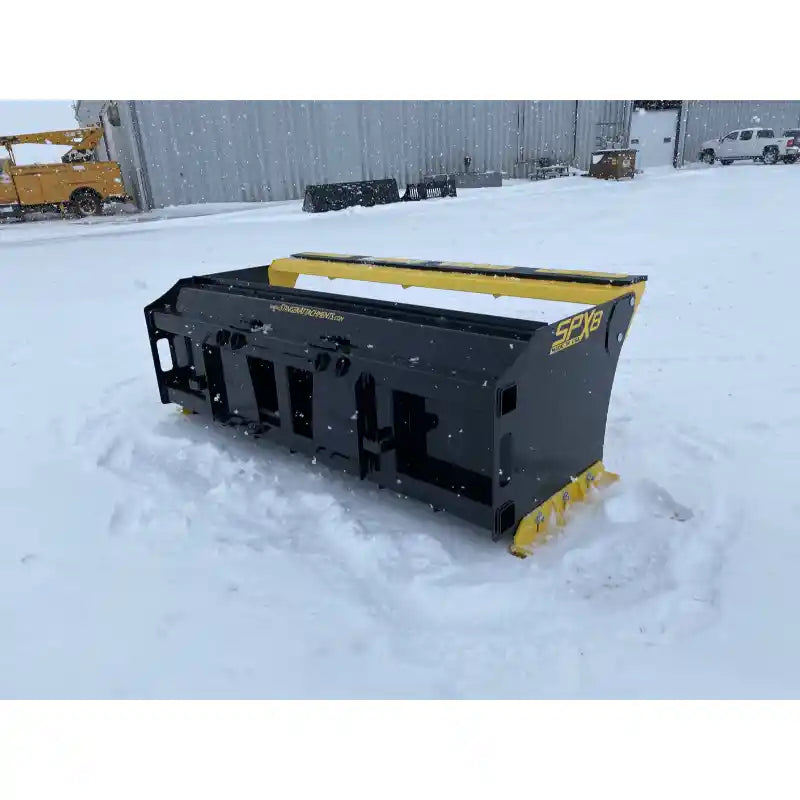 Rear right angle of black and yellow skid steer snow pusher attachment sitting on snow outside building