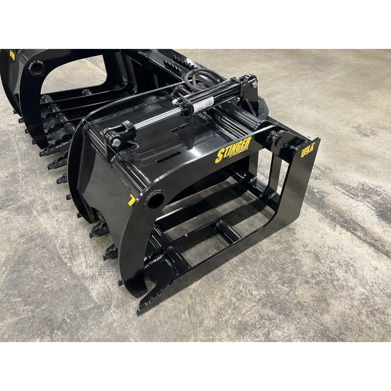 Black skid steer grapple attachment with solid hydraulic cylinder, curved tines, and reinforced steel frame on concrete floor