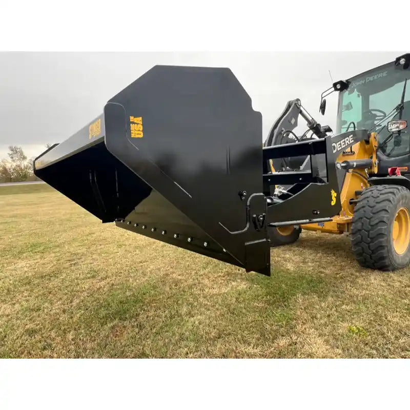 Right side view of black steel hydraulic dump bucket attached to front loader arm on yellow John Deere tractor on grass
