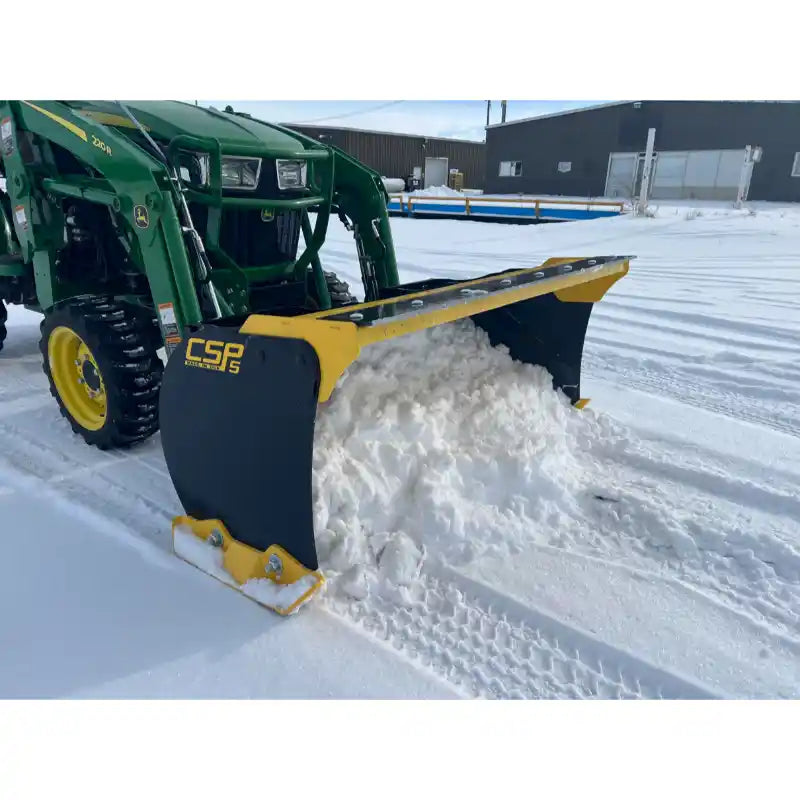 Yellow and black steel snow pusher attachment mounted on green tractor clearing snow on flat snowy surface