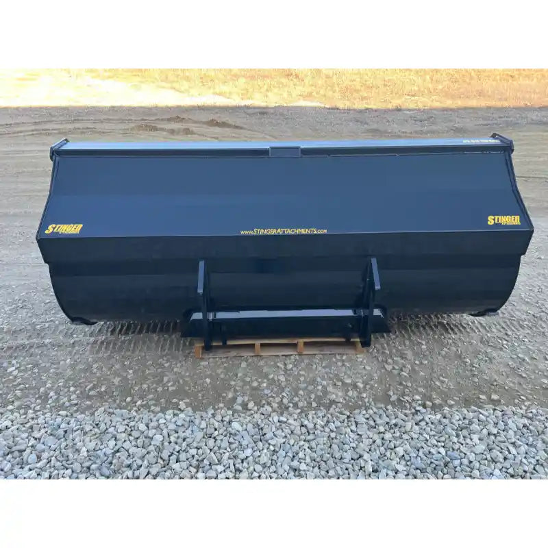Front view of black steel construction bucket attachment with smooth edges and yellow brand markings on gravel ground