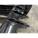 Close-up of black metal skid steer grapple attachment teeth with welded reinforcements on concrete surface