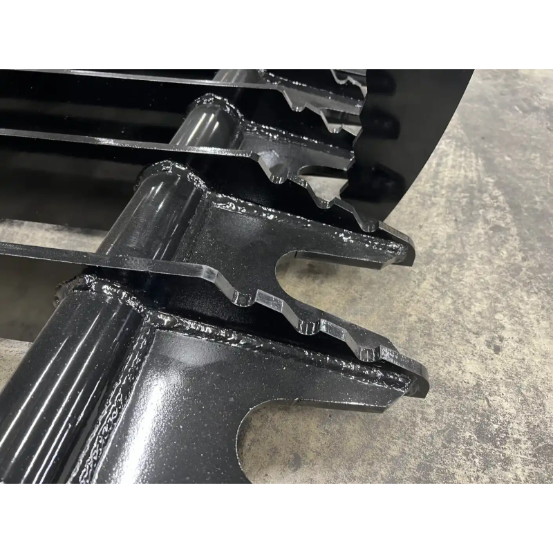 Close-up of black metal skid steer grapple attachment teeth with welded reinforcements on concrete surface
