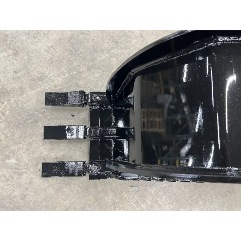 Black skid steer bucket attachment with three flat rectangular digging teeth and curved back on concrete floor