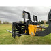 Black steel pallet fork attachment with vertical perforated backrest mounted on yellow skid steer arm over grassy field