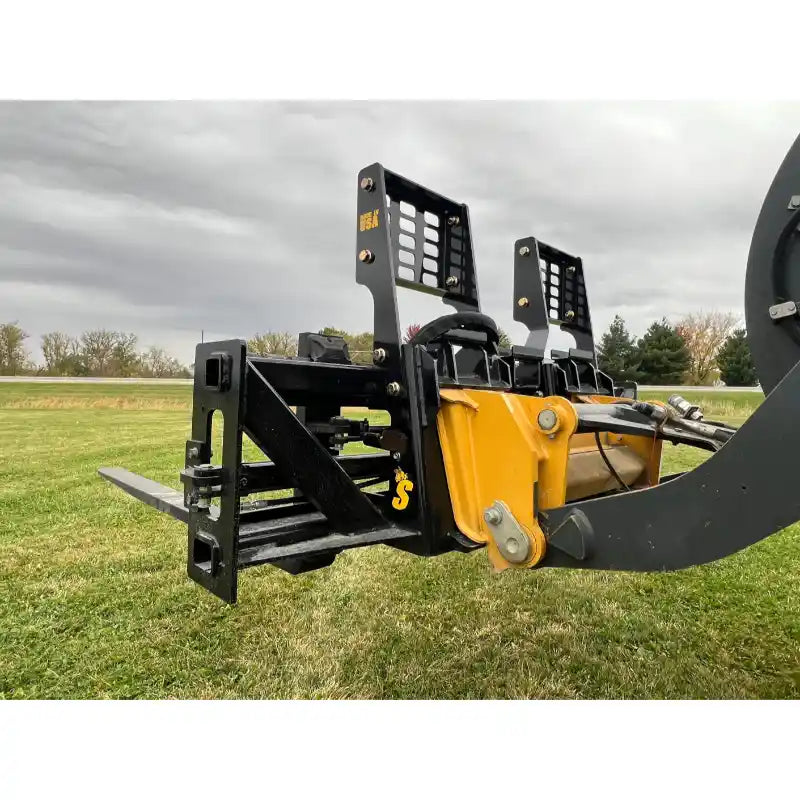 Black steel pallet fork attachment with vertical perforated backrest mounted on yellow skid steer arm over grassy field