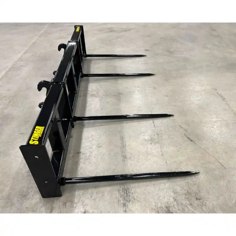 Black skid steer bale spear attachment with four pointed spears laid flat on concrete floor viewed from side angle