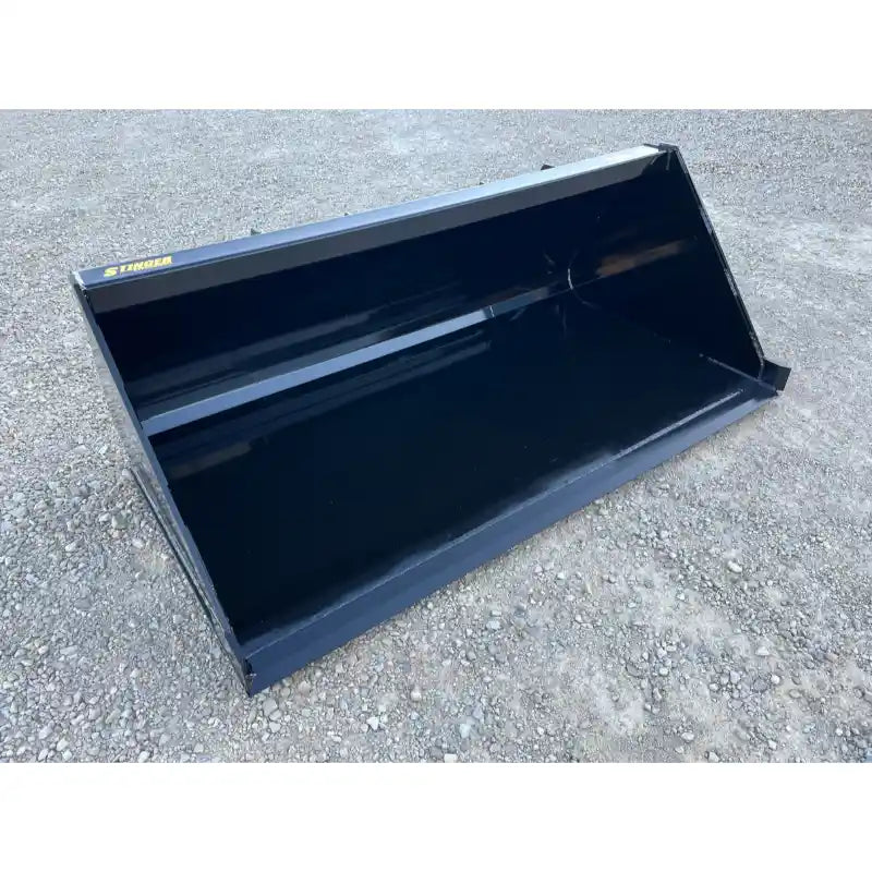 Front-right angle view of a black steel liquid slurry bucket attachment resting on gravel surface outdoors