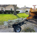 Black steel log dolly with turf tires loaded with cut tree logs beside a yellow wood chipper on gravel driveway