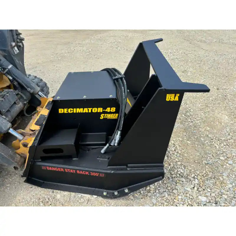 Black skid steer hydraulic mulcher attachment with hoses and safety warning label on gravel surface