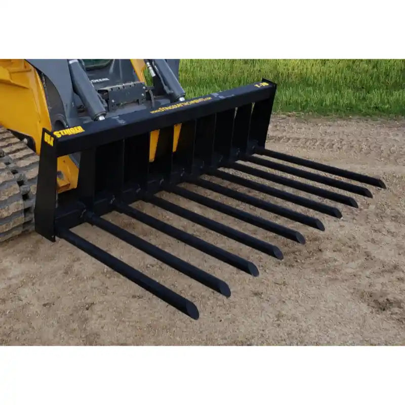 Black steel manure fork attachment with eleven evenly spaced, pointed tubular tines mounted on a skid steer loader outdoors